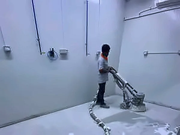 Worker grinding a concrete floor in a white room
