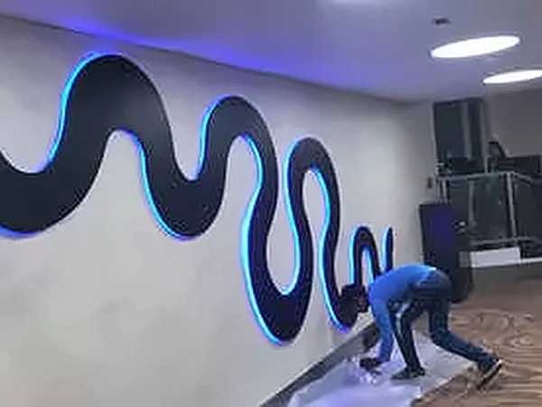 Wave-shaped wall artwork with blue LED edge lighting during installation